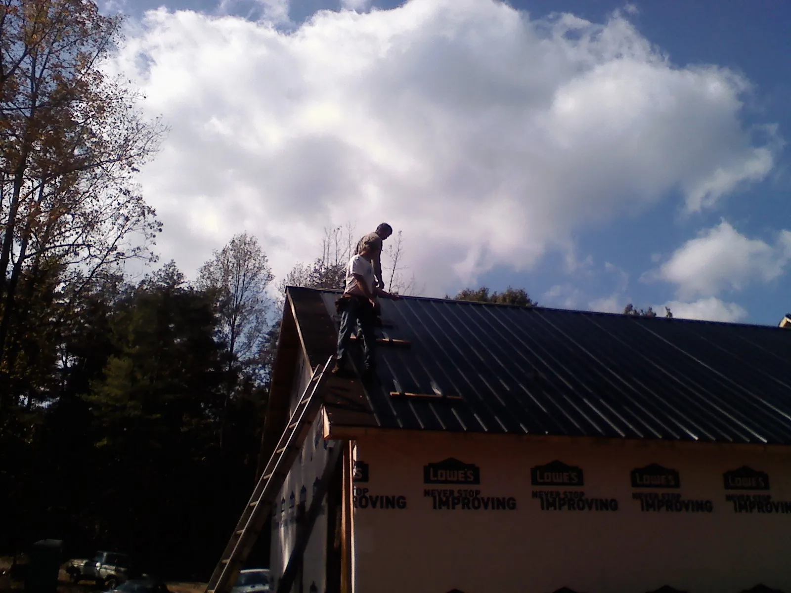 Roofer fastening dark metal panels high against a cloudy sky, from a Roof Inspection job in Duvall