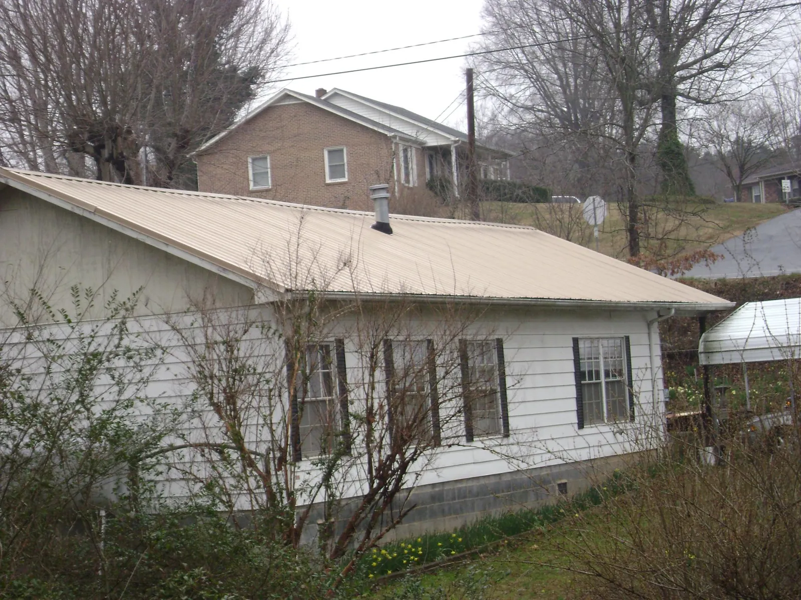 Tan metal roof on a white sided house set into a hillside — Commercial Roofing by Roofing Brothers in Duvall